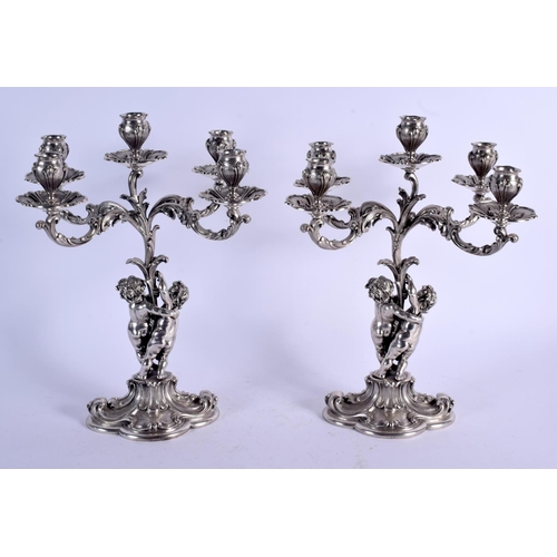 1157 - A LOVELY PAIR OF CONTINENTAL SILVER CANDLEABRA modelled two cherubs holding aloft floral capped scon... 