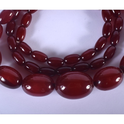 1002 - A 1930S CHERRY AMBER NECKLACE. 61 grams. 76 cm long, largest bead 2.75 cm wide.