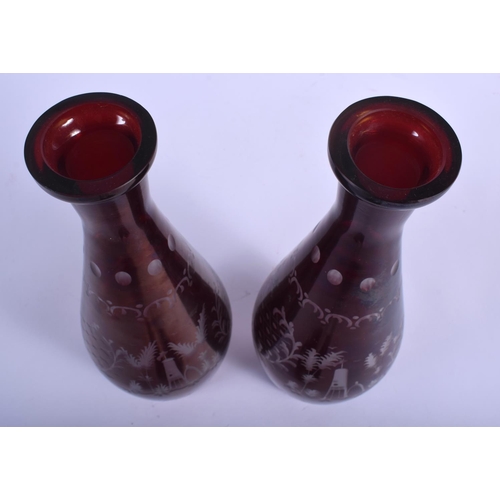 27 - A PAIR OF EARLY 20TH CENTURY BOHEMIAN RUBY GLASS DECANTERS AND STOPPERS decorated with deer and land... 