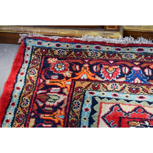 2601 - A LARGE MIDDLE EASTERN RED GROUND CARPET decorated with a blue lozenge of flowers. 354 cm x 264 cm.