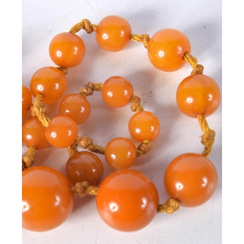 1032 - AN AMBER TYPE NECKLACE. 38 grams. 50 cm long, largest bead 1.5 cm wide.