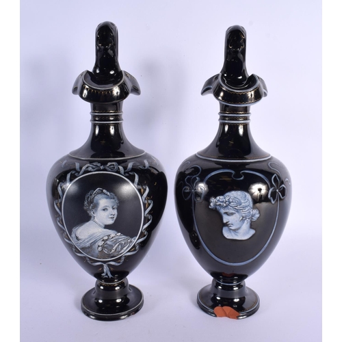 79 - A LARGE PAIR OF MID 19TH CENTURY ENGLISH BLACK POTTERY EWERS painted with portraits. 32 cm high.