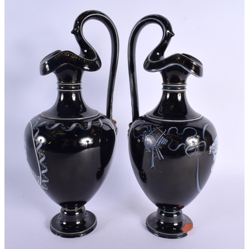 79 - A LARGE PAIR OF MID 19TH CENTURY ENGLISH BLACK POTTERY EWERS painted with portraits. 32 cm high.