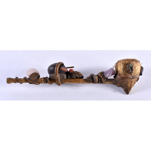 452 - AN UNUSUAL TRIBAL CARVED WOOD AND NUT GEM SET PIPE formed with a grotesque figure. 20 cm long.