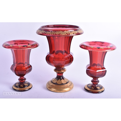 6 - A 19TH CENTURY BOHEMIAN RUBY GLASS GARNITURE painted in gilt with foliage and vines. Largest 14 cm x... 