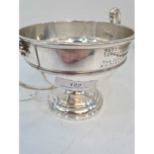 122 - A silver trophy cup on a raised pedestal circular base. Two handles with acanthus leaf detail. Bande... 