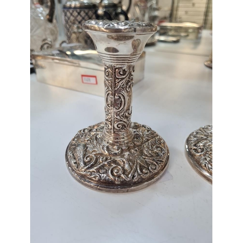 66 - A pair of decorative silver candlesticks, heavily embossed with foliate scrolls and a bird seated wi... 