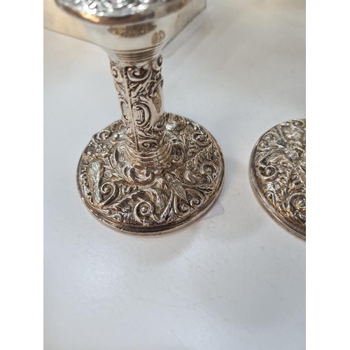 66 - A pair of decorative silver candlesticks, heavily embossed with foliate scrolls and a bird seated wi... 