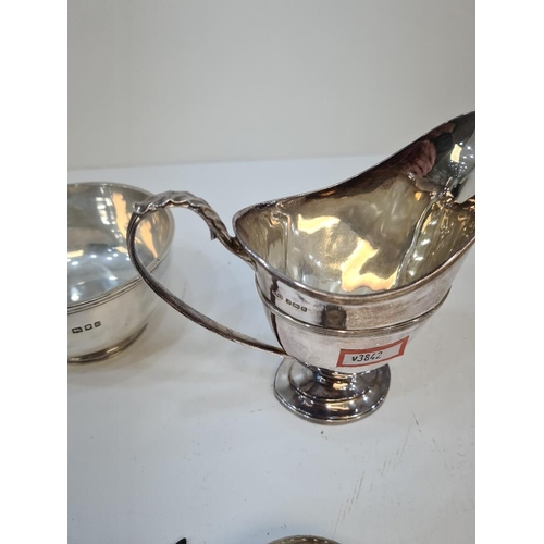 8A - A heavy silver sugar bowl, a silver milk jug with acanthus leaf handle, and a silver tea strainer, b... 