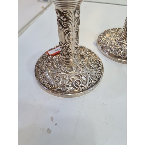 1123A - A pair of decorative silver candlesticks, heavily embossed with foliate scrolls and a bird seated wi... 