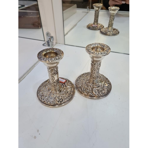 1123A - A pair of decorative silver candlesticks, heavily embossed with foliate scrolls and a bird seated wi... 