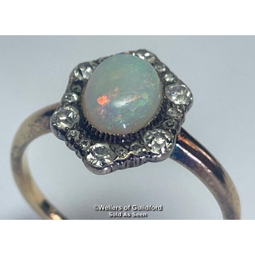 355 - Opal and diamond cluster ring. An oval opal surrounded by a border of old cut diamonds forming a hex... 