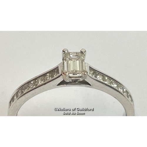 338 - An emerald cut diamond solitaire ring with diamond shoulders, in hallmarked 18ct white gold. Estimat... 