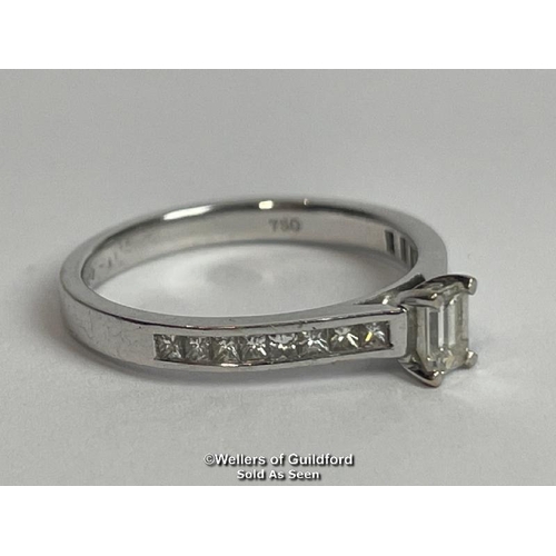 338 - An emerald cut diamond solitaire ring with diamond shoulders, in hallmarked 18ct white gold. Estimat... 