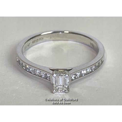 338 - An emerald cut diamond solitaire ring with diamond shoulders, in hallmarked 18ct white gold. Estimat... 