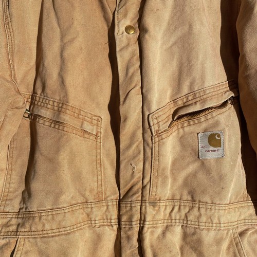 730 - Carhartt beige coverall features multiple pockets and snap closures.   / All lots are located at The... 