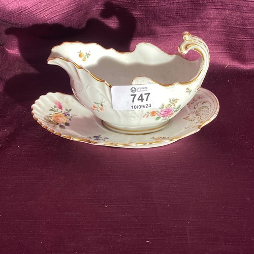 747 - A porcelain gravy boat with an attached underplate is showcased. It features gold accents and floral... 