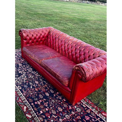 694 - A 20th century fully buttoned Chesterfield sofa in rich red leather hyde, repaired damage to one arm... 