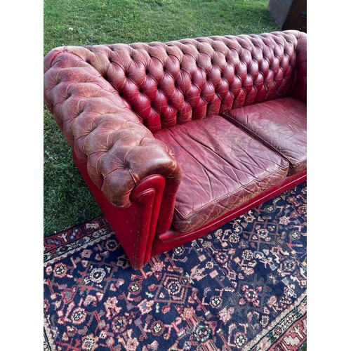 694 - A 20th century fully buttoned Chesterfield sofa in rich red leather hyde, repaired damage to one arm... 