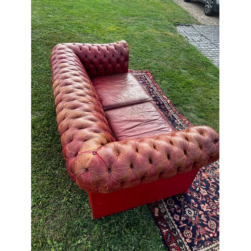 694 - A 20th century fully buttoned Chesterfield sofa in rich red leather hyde, repaired damage to one arm... 