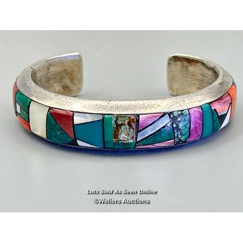 42 - A Native American inlaid stone bangle by Frank Yellowhorse, stamped Sterling, Novaro (as found), and... 