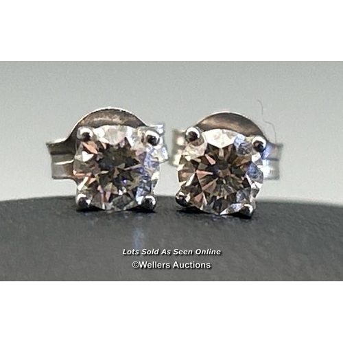 78 - A pair of solitaire diamond earrings in white metal, scrolls stamped 18ct. Estimated diamond weight ... 