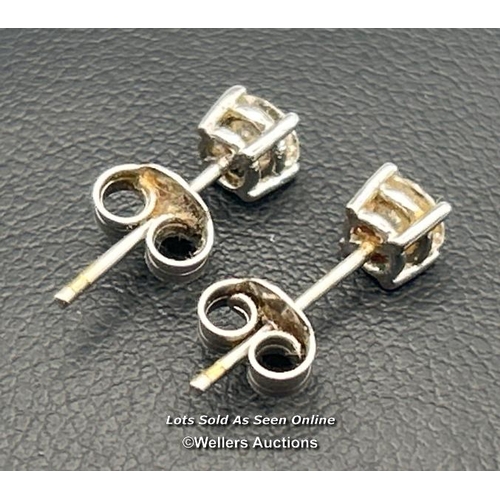 78 - A pair of solitaire diamond earrings in white metal, scrolls stamped 18ct. Estimated diamond weight ... 