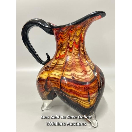 19 - A large heavy Murano style glass jug with amber, black and red tones on three legs, 23 cm high / T43