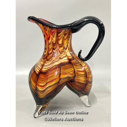 19 - A large heavy Murano style glass jug with amber, black and red tones on three legs, 23 cm high / T43