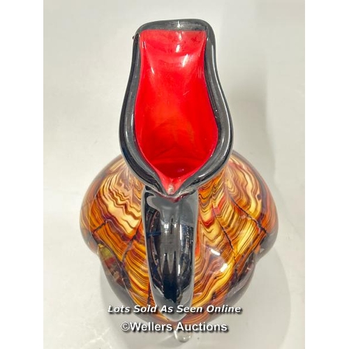 19 - A large heavy Murano style glass jug with amber, black and red tones on three legs, 23 cm high / T43