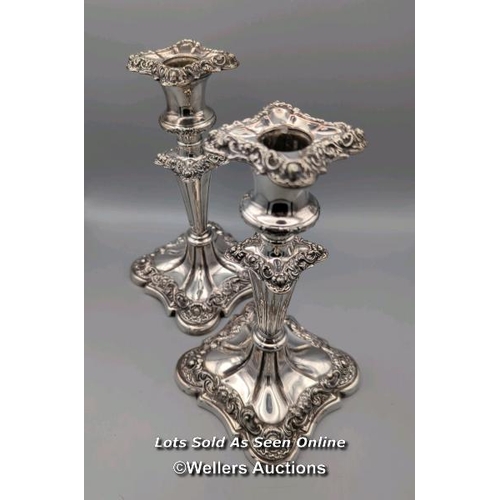 209 - A pair of silver plated candlesticks of a panelled V-stem design on square bases with ornate foliate... 