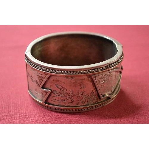 351 - Victorian oval hinged bangle, the front decorated with birds, a bat and sprays, in the Aesthetic Mov... 