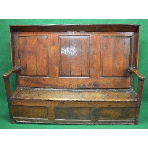 75 - Period oak settle having three panelled back supported by open arms leading to lift seat opening to ... 