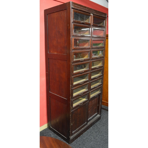 26 - Dudley & Co. mahogany stained haberdashery cabinet having sixteen glazed drawers over two sliding do... 