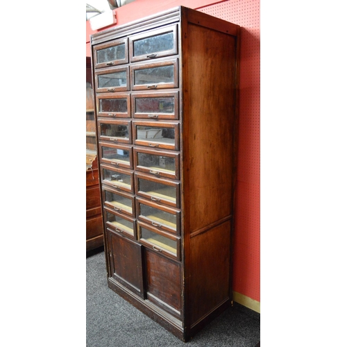 26 - Dudley & Co. mahogany stained haberdashery cabinet having sixteen glazed drawers over two sliding do... 