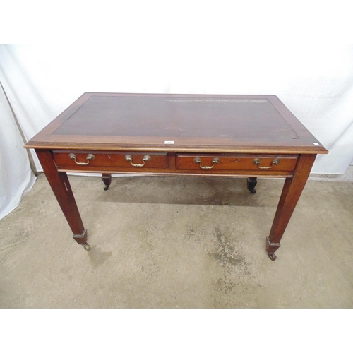 501 - Mahogany two drawer desk with inset top, standing on square tapering legs ending in castors.