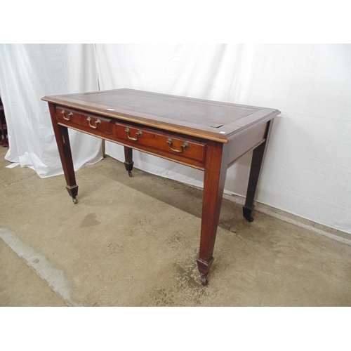 501 - Mahogany two drawer desk with inset top, standing on square tapering legs ending in castors.