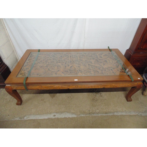 508 - Large deeply carved hardwood coffee table with glass top cover, the rectangular top having a scene w... 