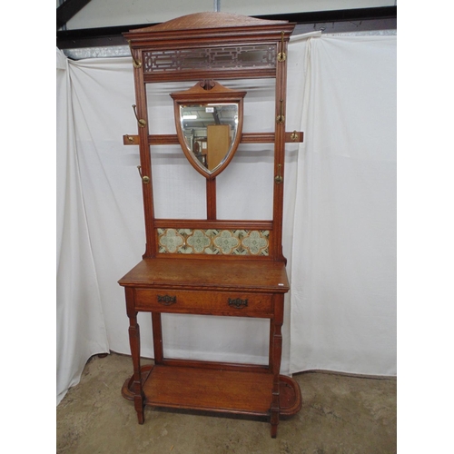 514 - Oak hall stand having pierced panel and shield shaped mirror flanked by six coat hooks above a tile ... 