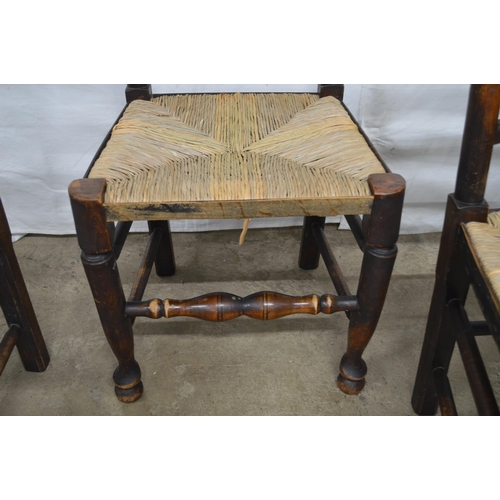 369 - Set of four oak ladderback chairs having rush seats, standing on turned front legs with stretchers -... 