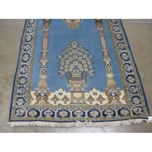 482 - Blue and cream ground patterned prayer rug having a central design with flowers in an urn flanked by... 