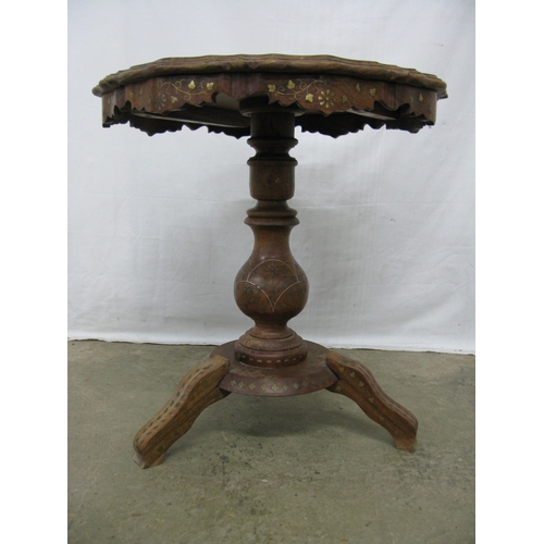 411 - Carved hardwood table having a shaped top with foliate brass inlay, standing on a turned column with... 