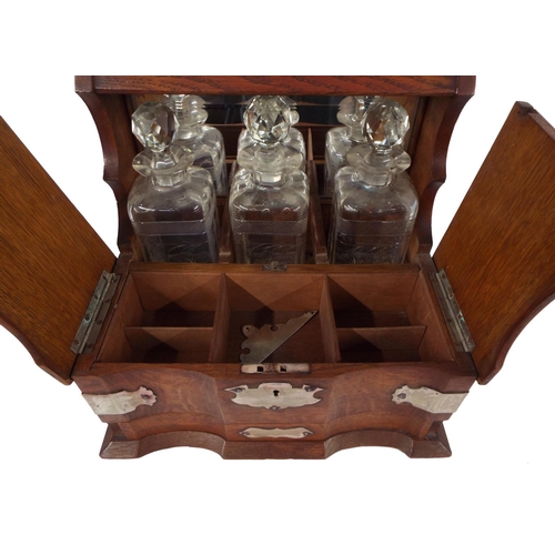 302 - Oak three bottle tantalus with silver plated mounts, the mirror back over a divided compartment and ... 