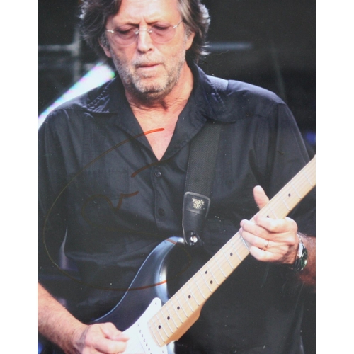 562 - Eric Clapton - autographed framed display, signed in red pen upon a photograph of Eric Clapton playi... 