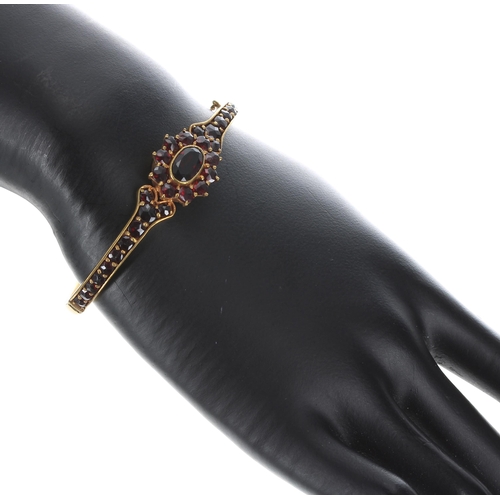 203 - Attractive garnet set cluster gilded bangle, with safety chain, 13.4gm