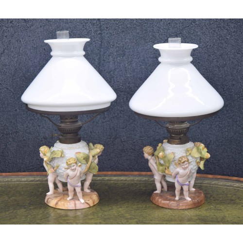 722 - Similar pair of Sitzendorf figural porcelain oil table lamps, modelled with cherubs supporting the w... 