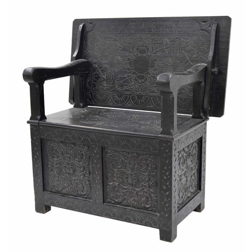 871 - Ebonised carved oak monk's bench, the transitional hinged top over a hinged seat enclosing an open b... 