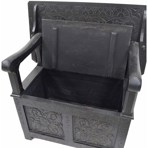 871 - Ebonised carved oak monk's bench, the transitional hinged top over a hinged seat enclosing an open b... 