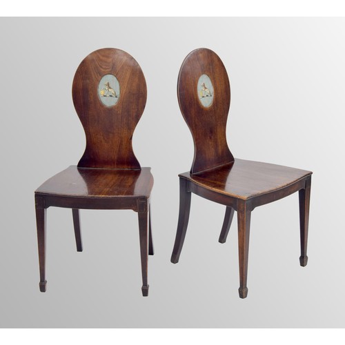 564 - Pair of 19th century mahogany hall chairs, the oval backs each with a recess panel painted with a co... 