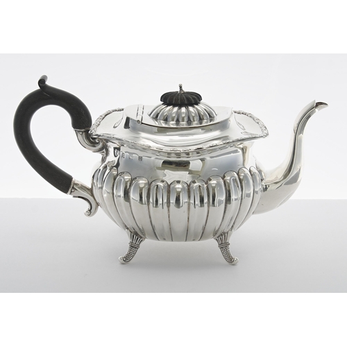 501 - George V silver teapot, with a hardwood handle and half gadrooned body raised on four scaled fe... 